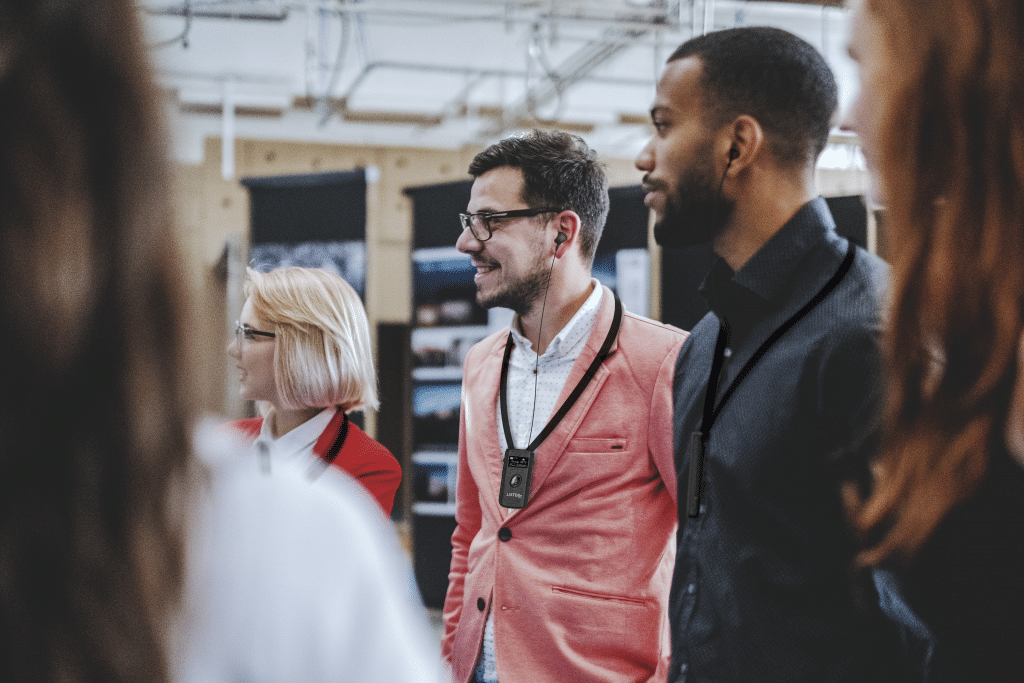 A group of adults wearing business casual clothing with Listen devices hanging on lanyards around their necks.