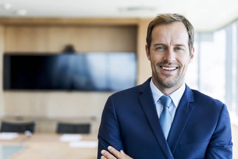 Portrait of confident mid adult businessman in board room. Business professional is standing in office. Male is smiling at workplace.