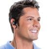 Headshot of a caucasian man with dark hair and brown eyes in a blue polo shirt with a big smile and wearing a LA-164 Universal Ear Speaker