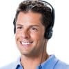 Middle aged man with dark hair wearing a blue collared shirt smiling while wearing over-the-head headphones