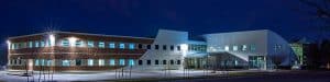 Listen Technologies two-story brick and stucco, brown and white Bluffdale office building at night, with an empty parking lot, the lights on inside, and a dark sky.