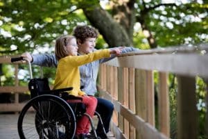 Frère aidant sa sœur dans un fauteuil roulant à l'extérieur