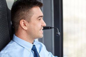 Vue latérale d'un homme ethnique séduisant d'une trentaine d'années avec des cheveux noirs et courts, des sourcils épais, portant une chemise bleue boutonnée avec une cravate bleu plus foncé, un chauffeur de bus avec un microphone installé
