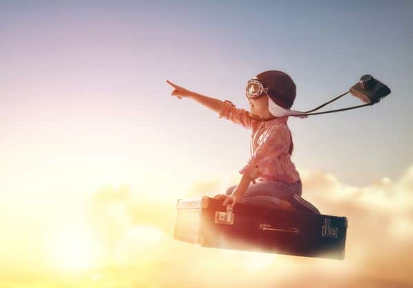 Bambino che usa l'immaginazione per viaggiare su una valigetta con casco, occhiali e macchina fotografica