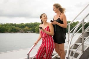 Zwei Frauen auf der Treppe einer Bootstour, die ihr Smartphone hören