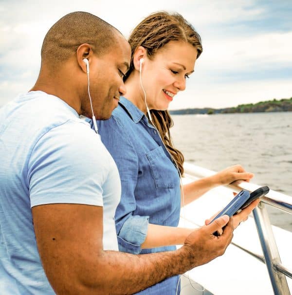 Couple on boat tour listening to audio through smartphone and earbuds