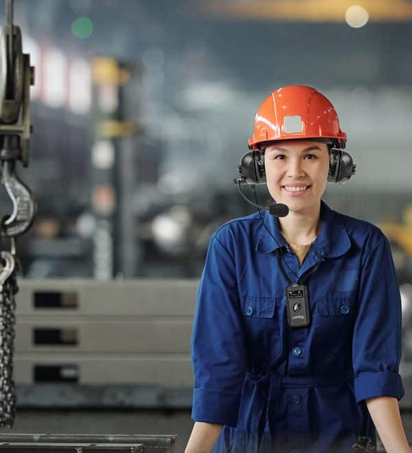 Cheerful young woman in workwear and protective helmet looking at you