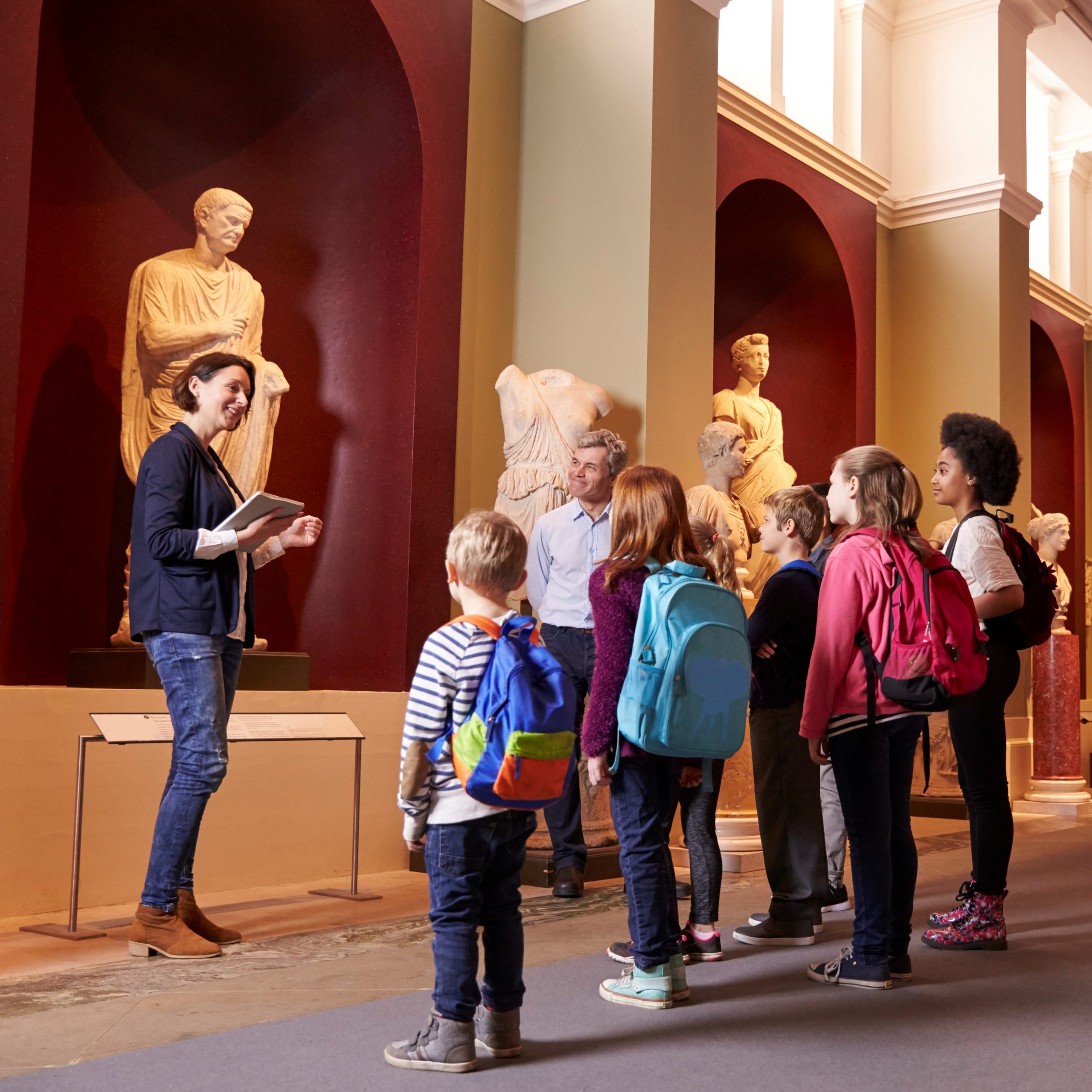 A group of young kids in an art museum, with a presenter talking to the children. 