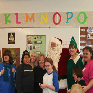 Listen Technologies employees and some teenagers posing with Santa in a classroom
