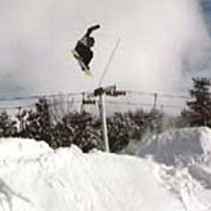 Snowboarder volando sobre la nieve en algún lugar de nieve profunda con el ascensor en el fondo