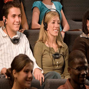 Two smiling people using headphones and assistive listening devices during a church service