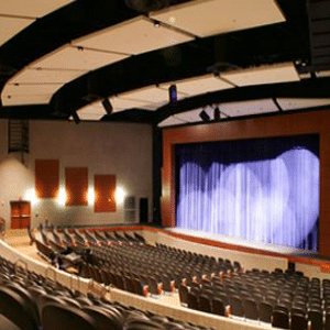 El interior de un teatro con un escenario iluminado y nadie sentado en los asientos.