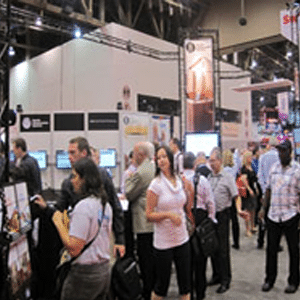 Piso de ferias comerciales ocupado y ruidoso con mucha gente y stands.