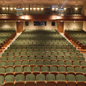 View of a community center from the stage looking out to empty rows of seating with a second tier of seating at the back of the room.