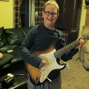 Niño sonriendo sosteniendo una guitarra en su sala de estar