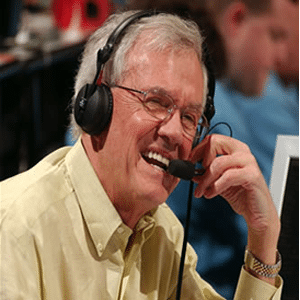 Close-up photo of Rodney Clark "Hot Rod" Hundley with a big smile and wearing a long-sleeved soft yellow button-down dress shirt, his wire frame oval shaped glasses, and a headset with a microphone