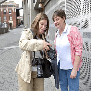 Two tourists outside while looking at the digital display of a camera to look at what was just photographed.