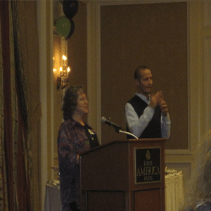 Two presenters inside a conference room presenting to a group.