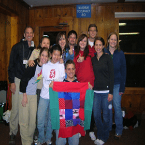 Group photo of smiling students huddled together holding up a quilt.