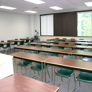 Salón con largas mesas rectangulares y sillas verdes estilo aula detrás de ellas con un podio en la parte delantera del salón.