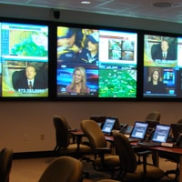Sala de conferencias con pantallas de televisión que muestran transmisiones de noticias.