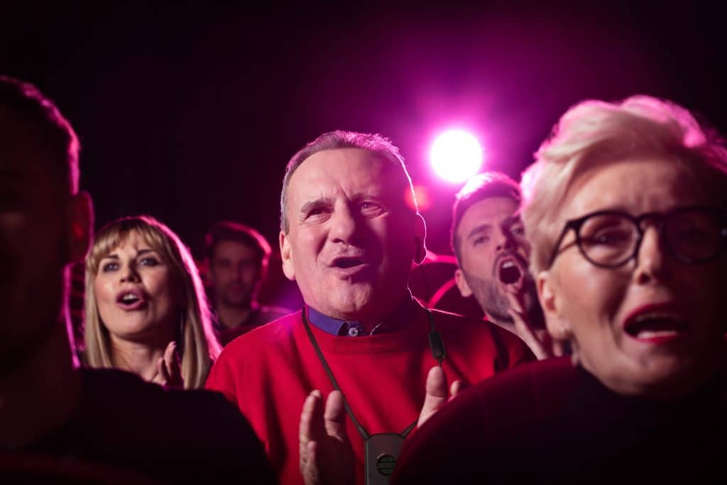 Group of happy people watching funny movie in the cinema. Senior man using assistive listening device.