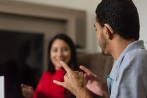 Hombre con problemas de audición, con audífonos, usando lenguaje de señas para comunicarse con una mujer vestida de rojo.