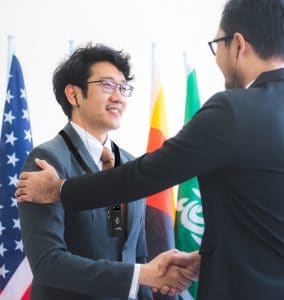 Hombre de negocios dándose la mano con un hombre frente a banderas internacionales.