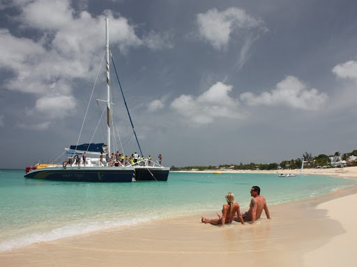 Couple d'âge moyen assis sur une plage tropicale en admirant un voilier entrant à terre.