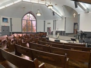 Side view of the inside of the sanctuary at Walnut Street Baptist Church with rows of empty pews and an art deco window.