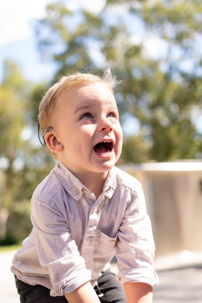 Happy young boy with a cochlear implant playing outside