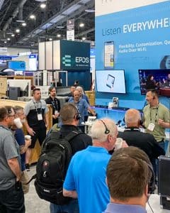 A tour group gathered at the Listen Technologies booth at InfoComm in 2022. Sam Nord is presenting and the group is wearing ListenTALK transceivers.