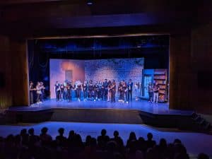 Estudiantes de secundaria vestidos de negro se paran frente al escenario en el teatro de la escuela secundaria John Rennie en Quebec, Canadá.