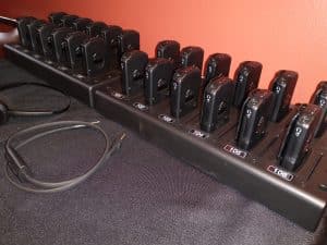 Two charging stands lined up with radio frequency (RF) assistive listening receivers in the charging slots and a neck loop on the counter next to the stand at the Lutcher Theater.