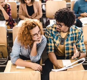 Due studenti indossano gli occhiali in un'aula con lo studente maschio che indossa un ricevitore di ascolto assistito a infrarossi su un cordino intorno al collo.