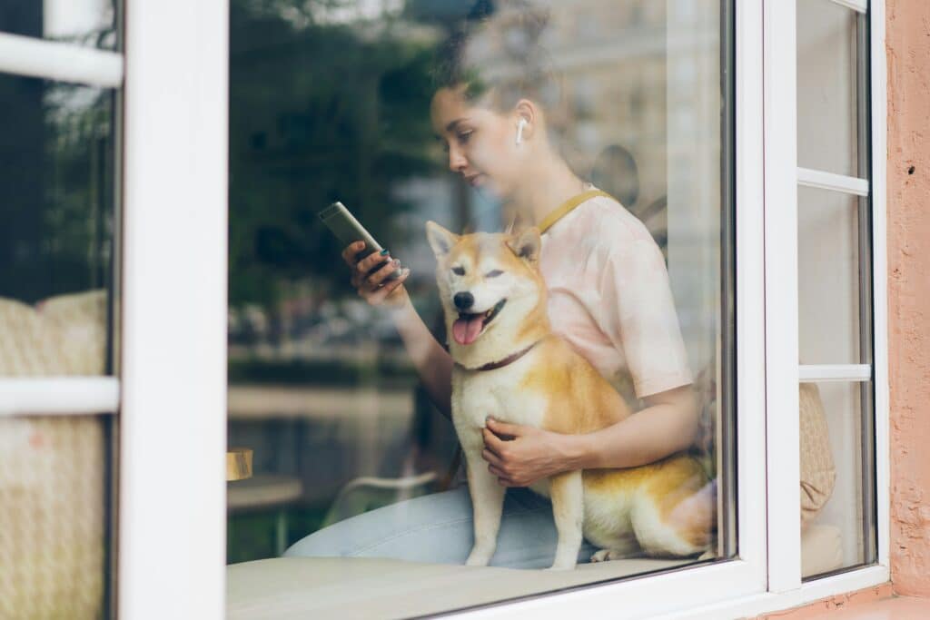 A picture of a women with her dog; she is looking at her phone and using headphones.